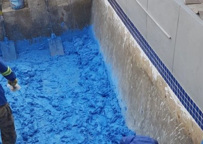 Sweeping the small concrete pools interior with blue sealant concrete primer.
