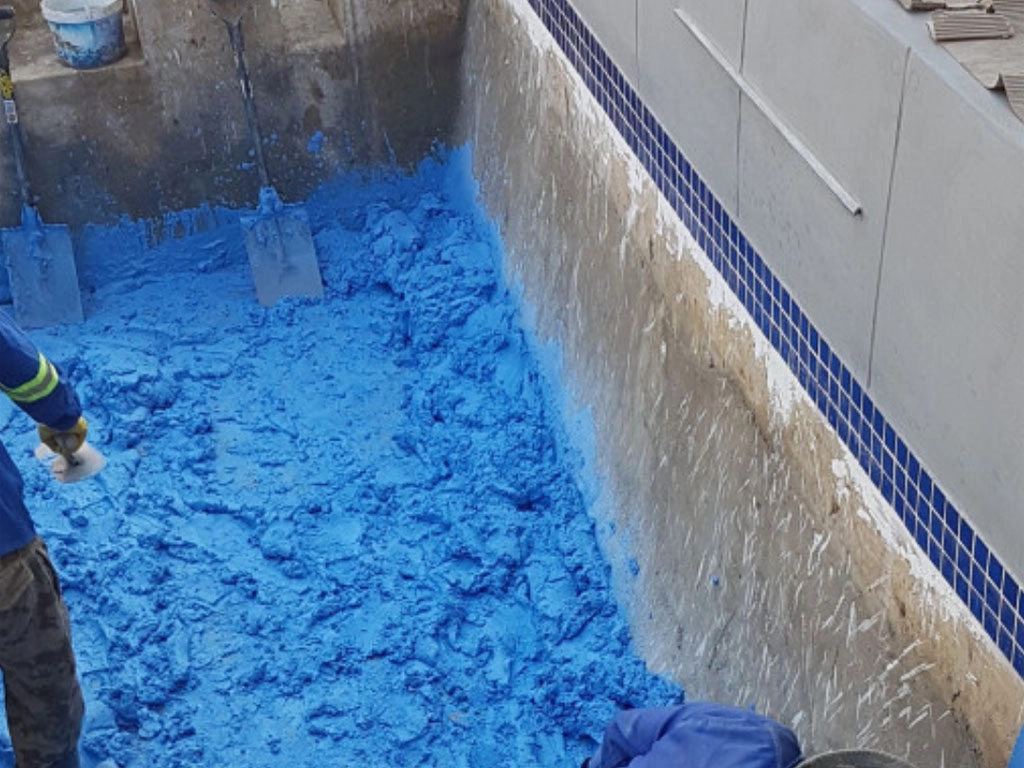 Sweeping the small concrete pools interior with blue sealant concrete primer.