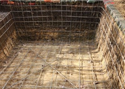 The construction process of a concrete pool, where only the hole has been dug, with the reinforcing wiring visible.