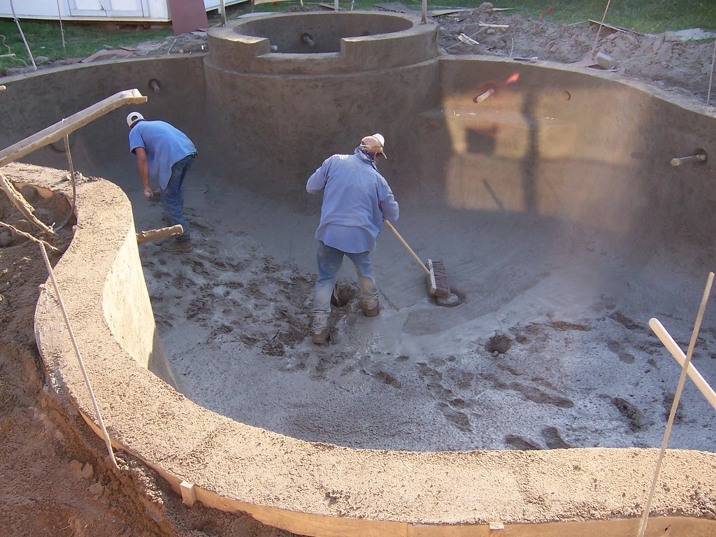 Concrete pool construction process, two guys sweeping the concrete floor of the swimming pool.